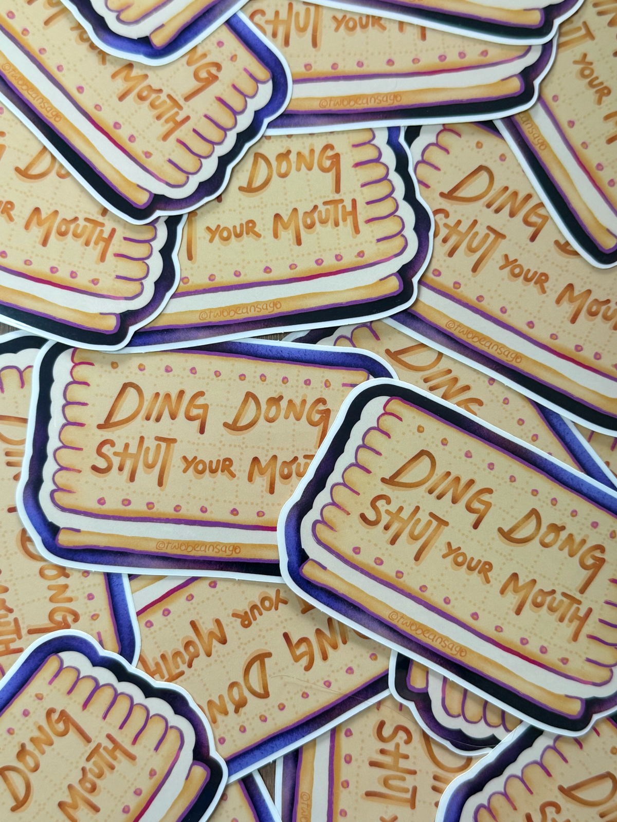 A pile of die-cut stickers shaped like golden-brown biscuits with the text 'DING DONG SHUT YOUR MOUTH'