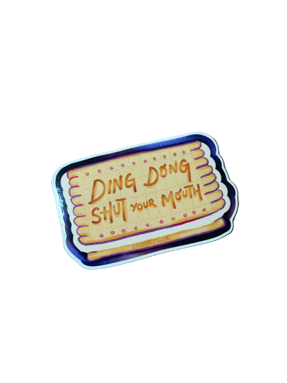 A die-cut sticker shaped like a biscuit with the text 'DING DONG SHUT YOUR MOUTH' 