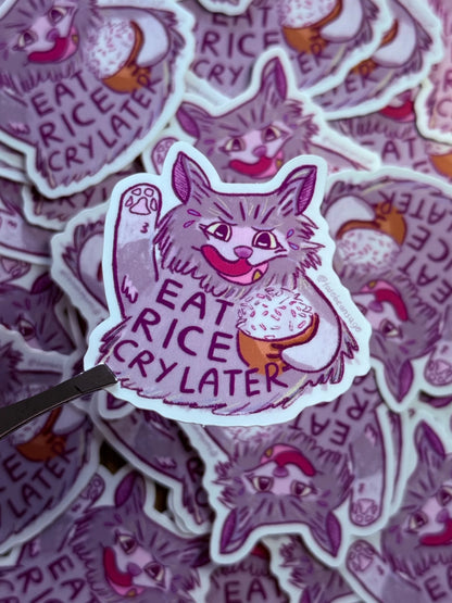 A die-cut sticker featuring a cartoon cat holding an ice cream cone with the text 'EAT RICE CRY LATER' 