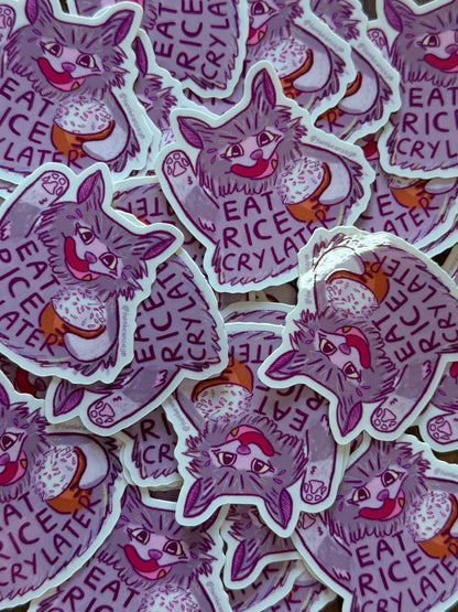 A pile of die-cut stickers featuring a purple cat illustration with the words 'EAT RICE CRY LATER' 