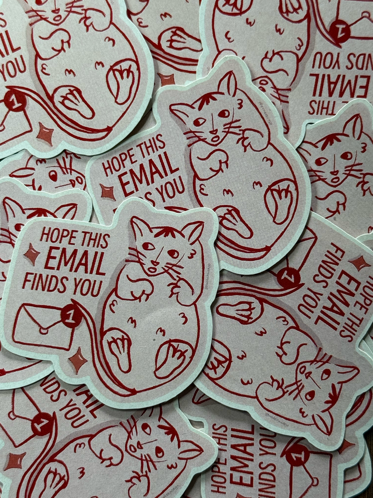 A pile of die-cut stickers featuring a red line-art cat sitting next to a red email icon and the text 'HOPE THIS EMAIL FINDS YOU'