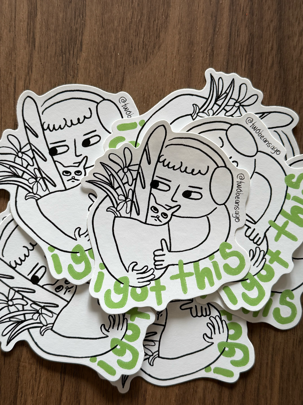 A pile of die-cut stickers featuring a black and white line art illustration of a person holding a rabbit, with green text reading 'I got this' 